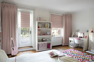 Les stores romains roses sont complétés par des rideaux roses assortis